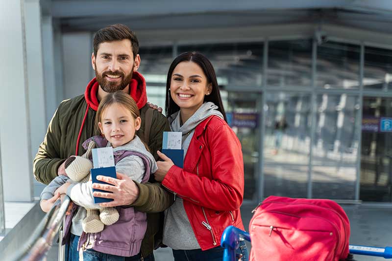 Portrait of the bearded father embracing his happy daughter while his wife standing nearby. Family waiting plane at the airport. Happy emotions concept